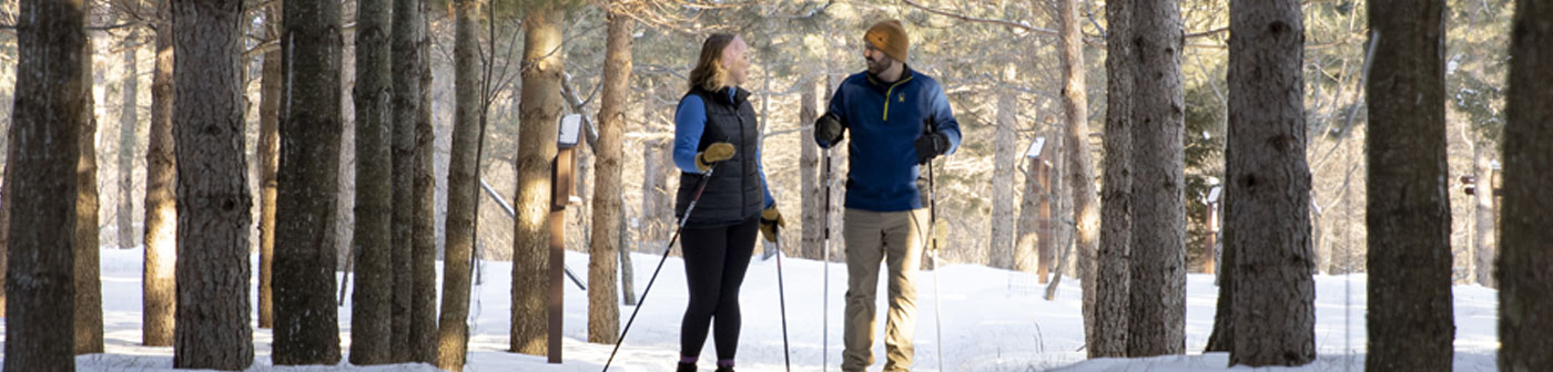 man and woman cross-country skiing through the trees